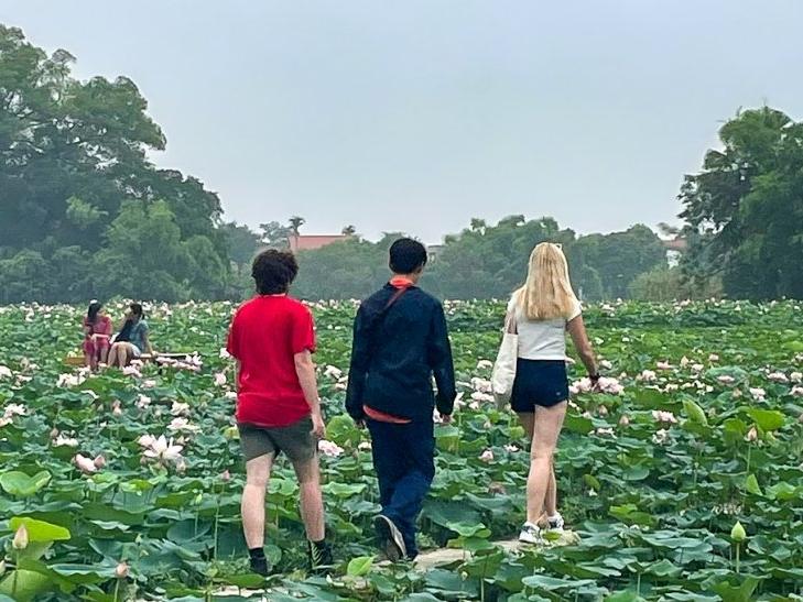 Three students walking through field of lily pads in Vietnam